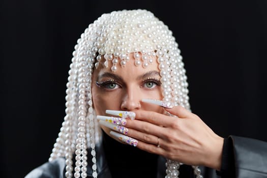 Studio portrait with back background of a woman with wig of pearls covering the mouth with hand