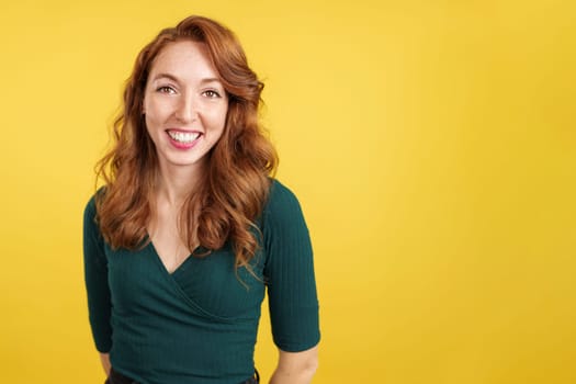Happy readheaded woman smiling at the camera in studio with yellow background