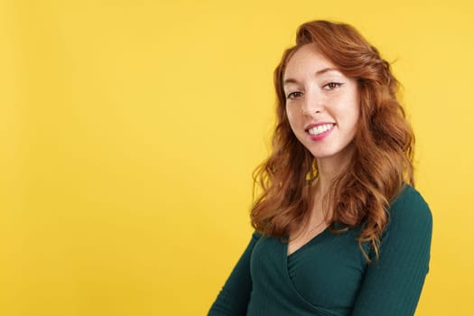 Cool redheaded woman looking at the camera relaxed in studio with yellow background
