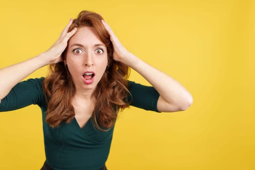 Surprised redheaded woman gesturing and looking at the camera in studio with yellow background