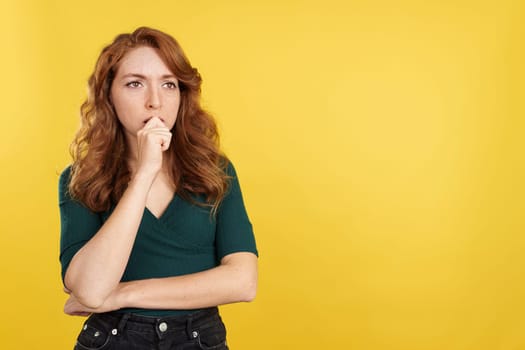 Redheaded woman with hand on face and thoughtful expression in studio with yellow background