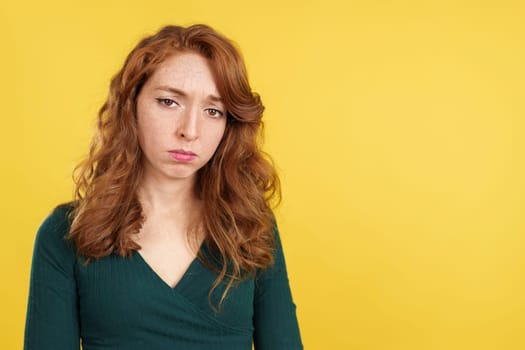 Redheaded woman looking down with sad expression in studio with yellow background