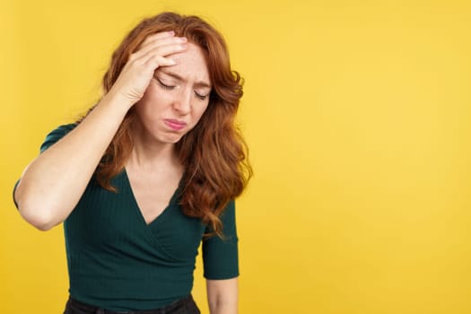 Beauty redheaded woman gesturing headache with the hand on head in studio with yellow background