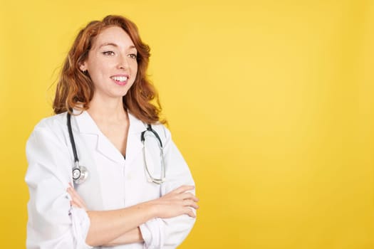 Friendly redheaded female doctor in uniform and stethoscope in studio with yellow background