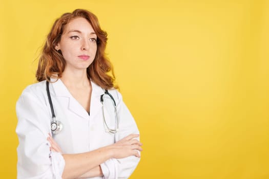 Serious redheaded female doctor with arms crossed looking away in studio with yellow background