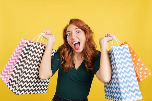 Redheaded woman happy with shopping in the sales in studio with yellow background