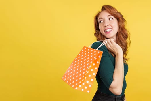 Smiley redheaded woman with a shopping bag in studio with yellow background