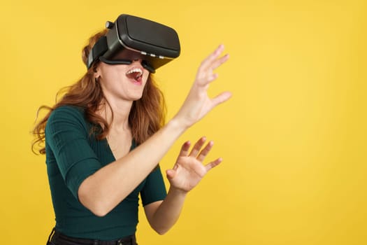 Happy redheaded woman with Virtual Reality goggles in studio with yellow background