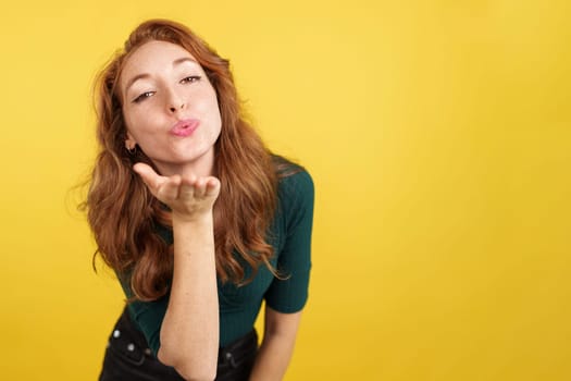 Redheaded woman blowing a kiss while looking at the camera in studio with yellow background