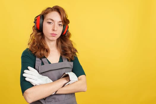 Serious redheaded female worker standing with arms crossed looking at camera in studio with yellow background