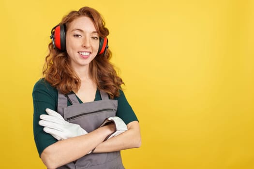 Friendly redheaded woman carpentry worker in work uniform in studio with yellow background
