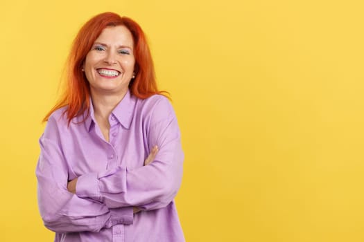 Happy mature woman laughing and looking at the camera in studio with yellow background