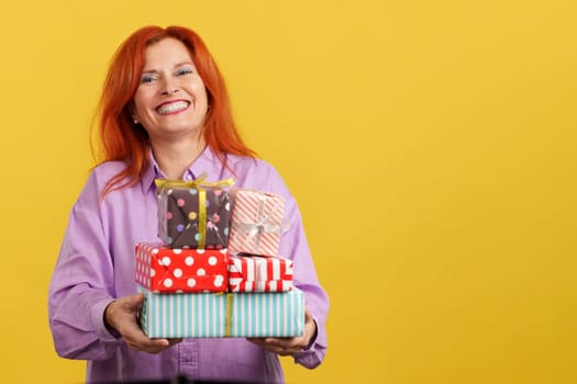 Happy redheaded mature woman receiving gifts for the mother's day in studio with yellow background