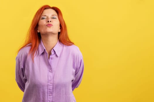 Redheaded mature and affectionate mother throwing a kiss to the camera in studio with yellow background