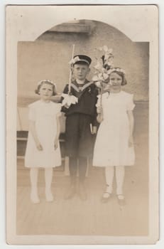 THE CZECHOSLOVAK REPUBLIC - CIRCA 1930s: Vintage photo shows children pose outside. The boy wears a sailor costum, the girls wear white dress. Retro black and white photography.