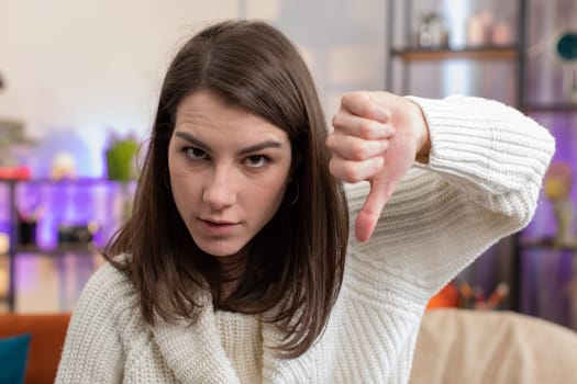 Dislike. Portrait of upset woman showing thumbs down sign gesture, expressing discontent, disapproval dissatisfied bad work at modern home apartment indoors. Displeased girl in living room on sofa