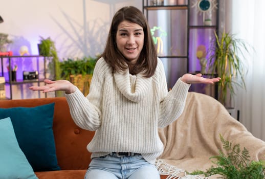 What. Why. Woman raising hands in indignant expression asking reason of failure demonstrating disbelief irritation by troubles at modern home apartment. Portrait of girl in living room sitting on sofa