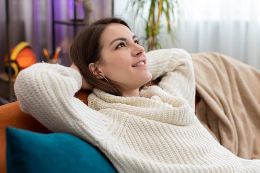 Portrait of tired young woman enjoy relaxing on home couch in room. Happy pretty girl lying on couch resting napping after hard working day, closed her eyes, put hands behind head, stress free, rest