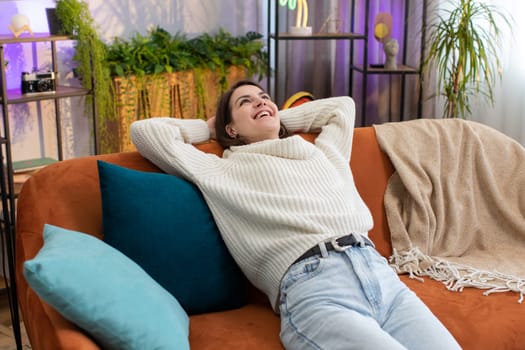 Portrait of tired young woman enjoy relaxing on home couch in room. Happy pretty girl lying on couch resting napping after hard working day, closed her eyes, put hands behind head, stress free, rest