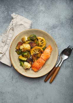 Delicious salmon fillet with grilled Brussels sprouts on plate, rustic stone background top view. Healthy dinner with grilled fish and vegetables, balanced nutrition