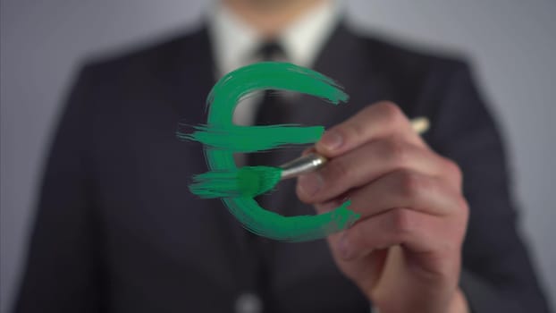 Businessman draws the euro symbol on the glass. A man in a suit draws on glass with a brush and green paint. 4k