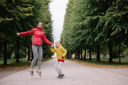 Mother and son jumping in the autumn park. Fall Season. Happy young beautiful mother and her son have a walk in the park