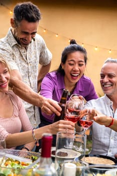 Vertical portrait of asian young woman toasting with wine, celebrating with friends, laughing during garden barbecue dinner party. Lifestyle concept.
