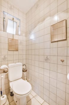 a white toilet in a bathroom with tile on the floor and wall behind it, there is a mirror above the toilet