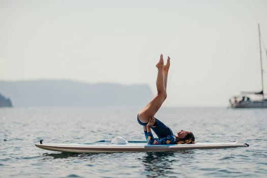 Woman sup yoga. Middle age sporty woman practising yoga pilates on paddle sup surfboard. Female stretching doing workout on sea water. Modern individual hipster outdoor summer sport activity