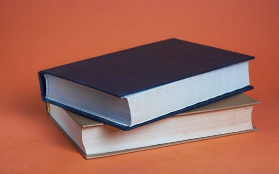 Two hardcover books on top of each other on a brown background. White and black book.