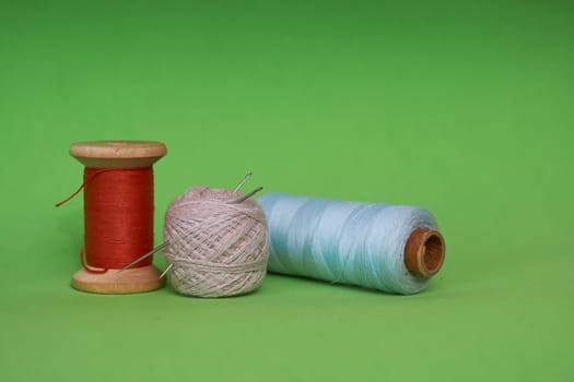 Multicolored needles with threads on a green background. The concept of advertising a sewing studio and stylist-designer courses