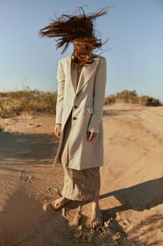 a stylish woman in fashionable summer clothes stands in the sand against a blue sky with her face covered by her hair. High quality photo