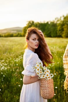 close portrait of a happy woman looking at the camera in a light dress and a wicker basket in her hands with chamomile flowers in nature. High quality photo