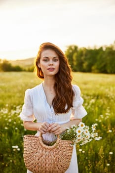 close portrait of a happy woman looking at the camera in a light dress and a wicker basket in her hands with chamomile flowers in nature. High quality photo