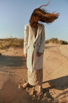 a stylish woman in fashionable summer clothes stands in the sand against a blue sky with her face covered by her hair. High quality photo