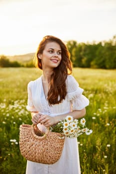 close portrait of a happy woman looking at the camera in a light dress and a wicker basket in her hands with chamomile flowers in nature. High quality photo