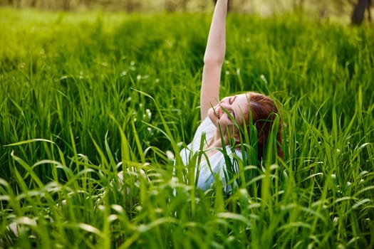 a cute woman in the summer high grass sits in a light dress happily raising her hand up. High quality photo