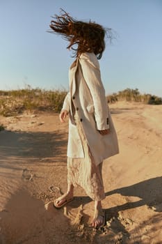 a stylish woman in fashionable summer clothes stands in the sand against a blue sky with her face covered by her hair. High quality photo