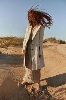 an atypical portrait of a woman in stylish summer clothes stands on the sands with hair covering her face. High quality photo