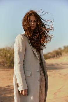 a beautiful woman in a light jacket looks at the camera while standing in nature and the wind blows her hair. High quality photo