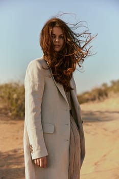 a beautiful woman in a light jacket looks at the camera while standing in nature and the wind blows her hair. High quality photo