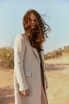 a beautiful woman in a light jacket looks at the camera while standing in nature and the wind blows her hair. High quality photo