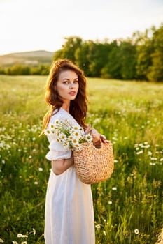 close portrait of a happy woman looking at the camera in a light dress and a wicker basket in her hands with chamomile flowers in nature. High quality photo