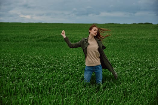 a woman stands in a field in cloudy weather and strong wind facing the camera with her hand raised up. High quality photo