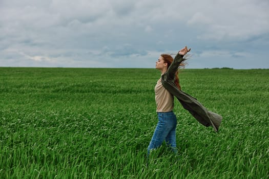 a woman in a long coat stands in tall green grass in a field, in cloudy weather, enjoying nature and the view. High quality photo