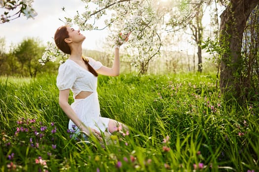 a woman in a light dress sits in the grass near a flowering apple tree. High quality photo