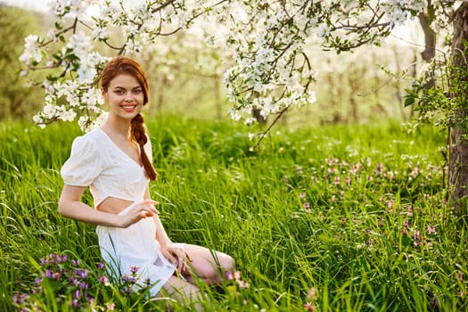 a young woman in a light summer dress is resting sitting under a flowering tree. High quality photo