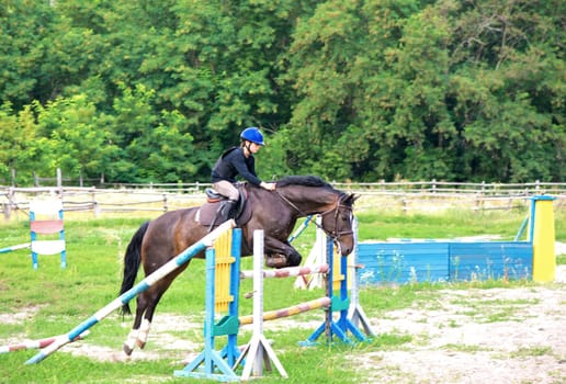 Young rider on horse jumping over obstacle on her course in competition