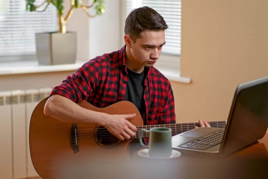 Relaxed man playing the guitar at home and using a laptop