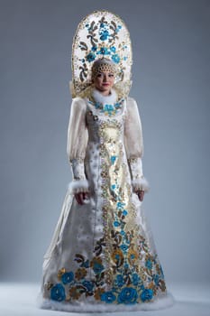 Pretty young girl in Russian costume and kokoshnik posing on blue background